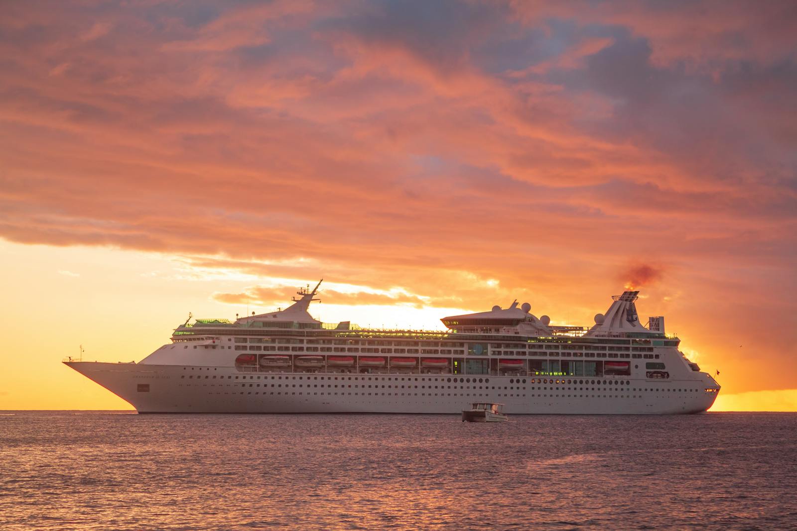 A cruise ship at anchor beneath a blazing pink sunset