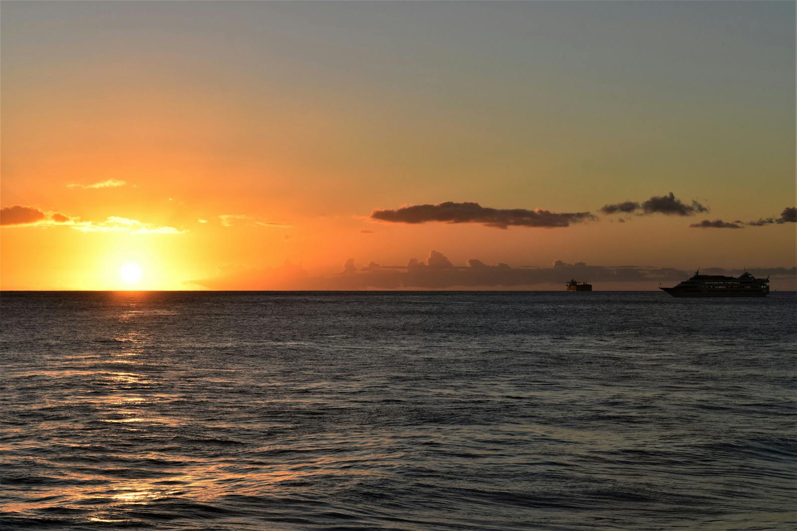 A quiet ocean horizon with distant ships under a glowing sunset