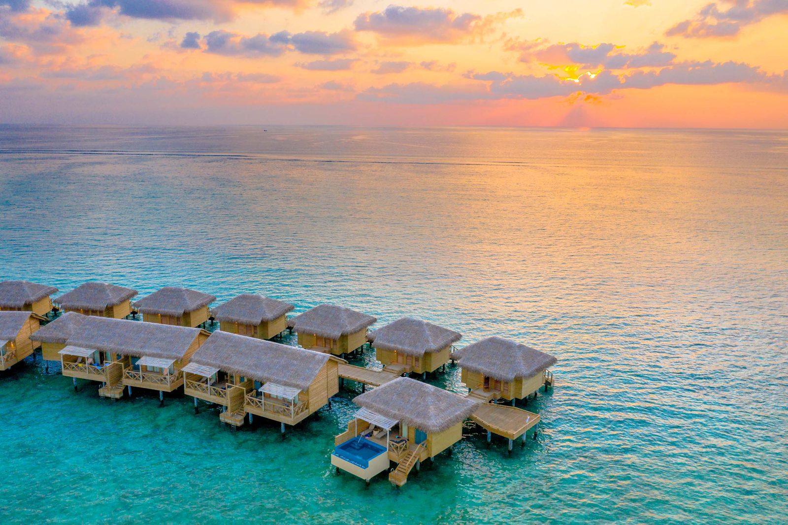 Overwater villas glowing under a pink and gold sunset